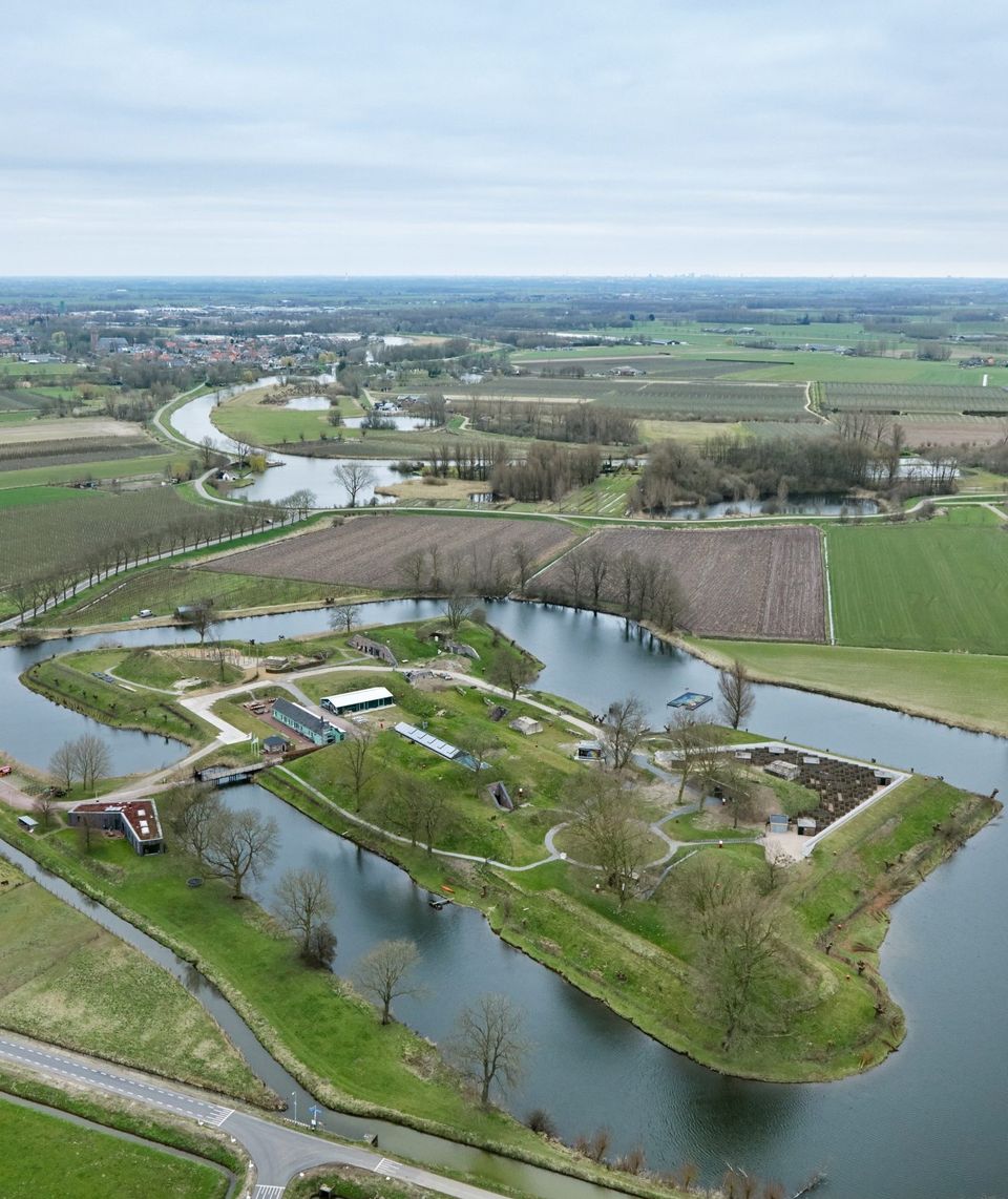 Een fort overgroeid met gras en omgeven door een fortgracht, gefotografeerd vanuit de lucht.
