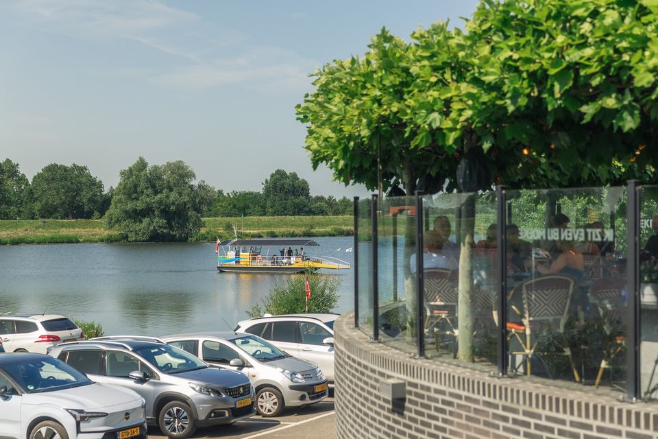 Auto's op een parkeerplaats op de oever naast de Rijn en naast Moeke in Rhenen.