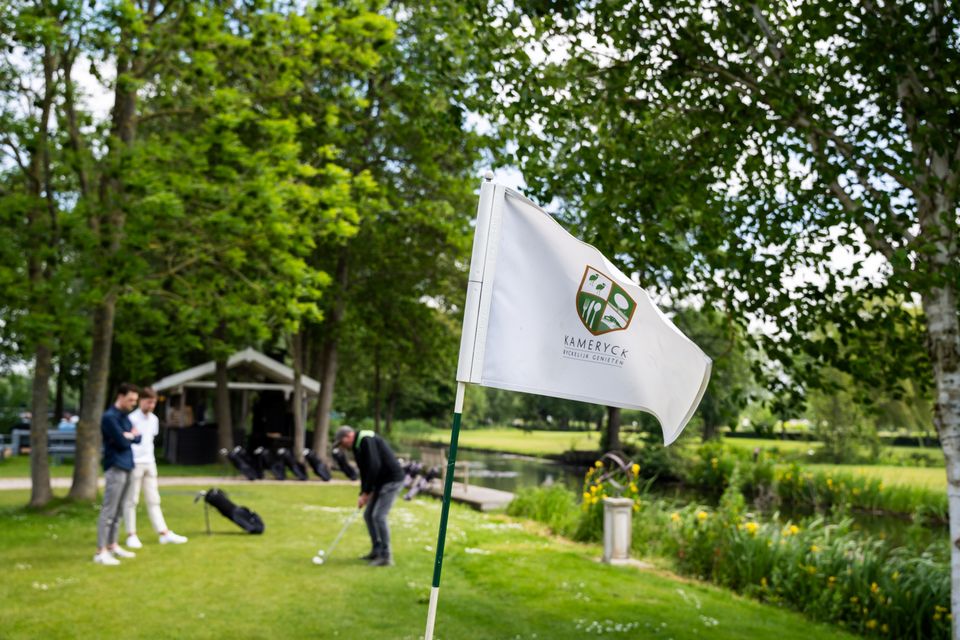 Golfvlag van Kameryck vooraan in beeld met deelnemers aan een golfclinic op de groene baan van Buitenplaats Kameryck