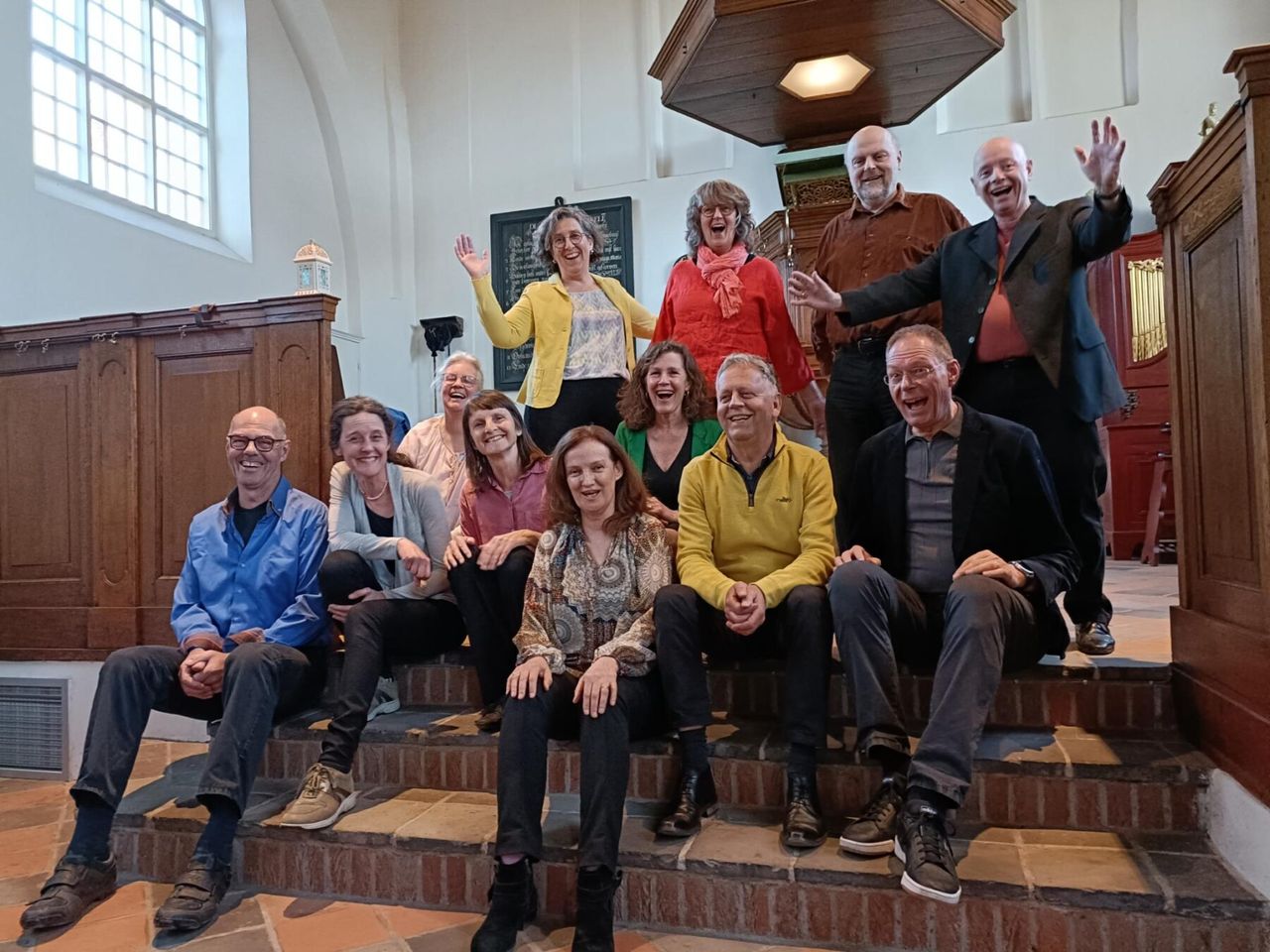 De 12 leden van zangensemble Innervoice zitten op de trap in het Lodewijkskerkje
