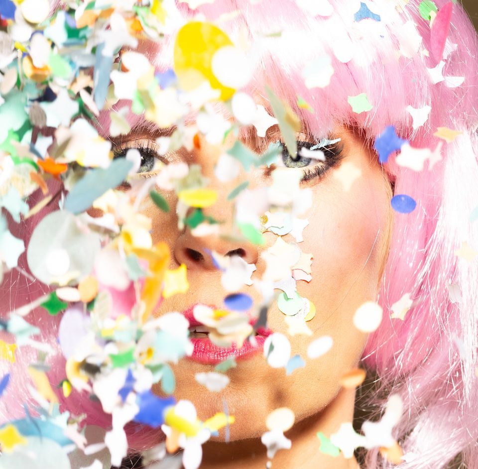 Vrouw met roze pruik en confetti voor haar gezicht