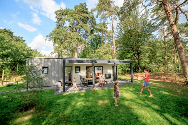 Vader en dochter spelen in de ruime tuin van chalet Zuylestein bij RCN het Grote Bos. Het moderne vakantiehuis ligt op een groene en bosrijke plek.