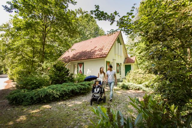 Een huisje op het vakantiepark waar een jong gezin met buggy langsloopt.