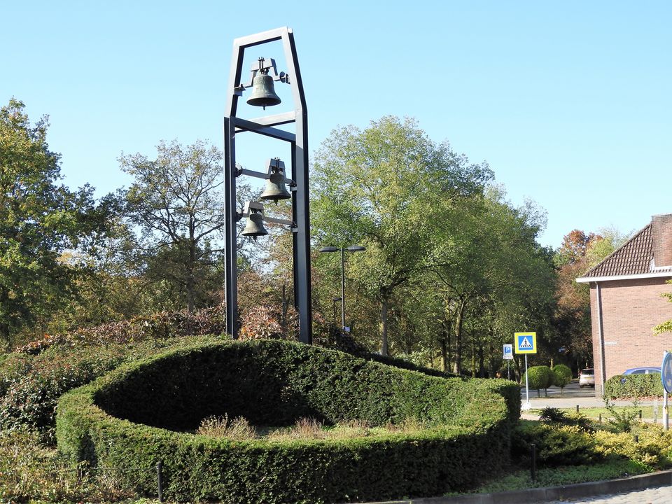 Ein begrünter Kreisverkehr, auf dem ein Metallgestell mit Glocken steht.