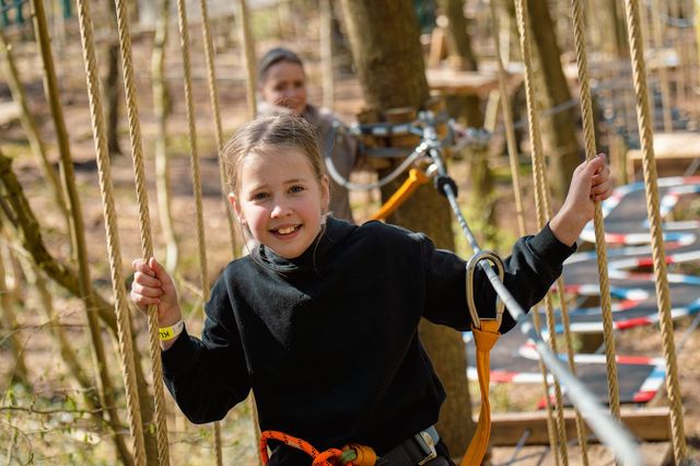 Ein junges Mädchen klettert über einen Parcours in einem Kletterwald in Drenthe, Niederlande.
