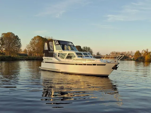 Motorjacht De Capella van REM Yachtcharter op het water met een laaghangende zon.