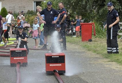 Evenement Brandweermiddag en Huttenbouw in Kamerik, Groene Hart. Kinderen spuiten met brandslangen tijdens een brandweeractiviteit onder begeleiding van de Brandweer Woerden, met toeschouwers langs het parcours tijdens een zomers familie-evenement.
