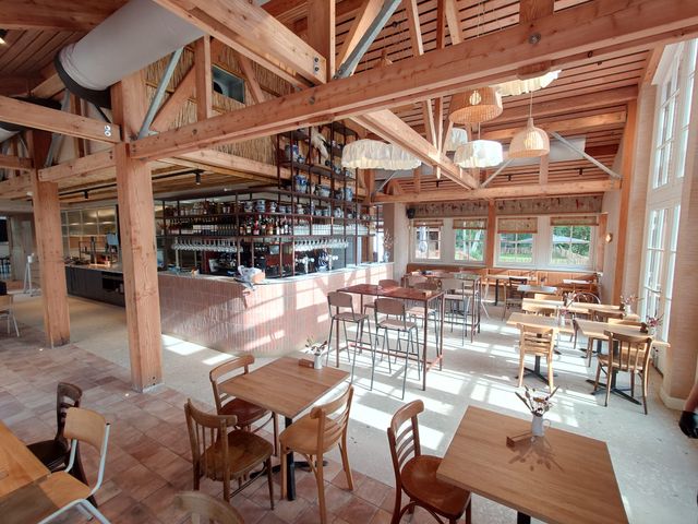 Restaurant De Oortjeshoeve in Kamerik, Groene Hart. Warm restaurantinterieur met houten spanten, centrale bar, open keuken en zitplaatsen in een karakteristieke boerderijsetting.