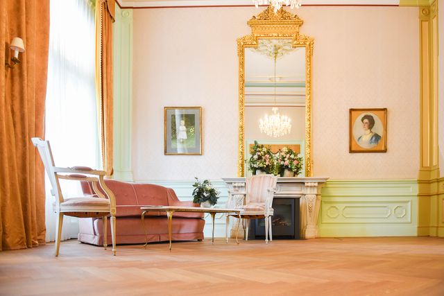 Binnenin de Vorstelijke Wachtkamer in Baarn. Er staat een stoel, hangt een lamp en het geheel heeft een chique uitstraling.