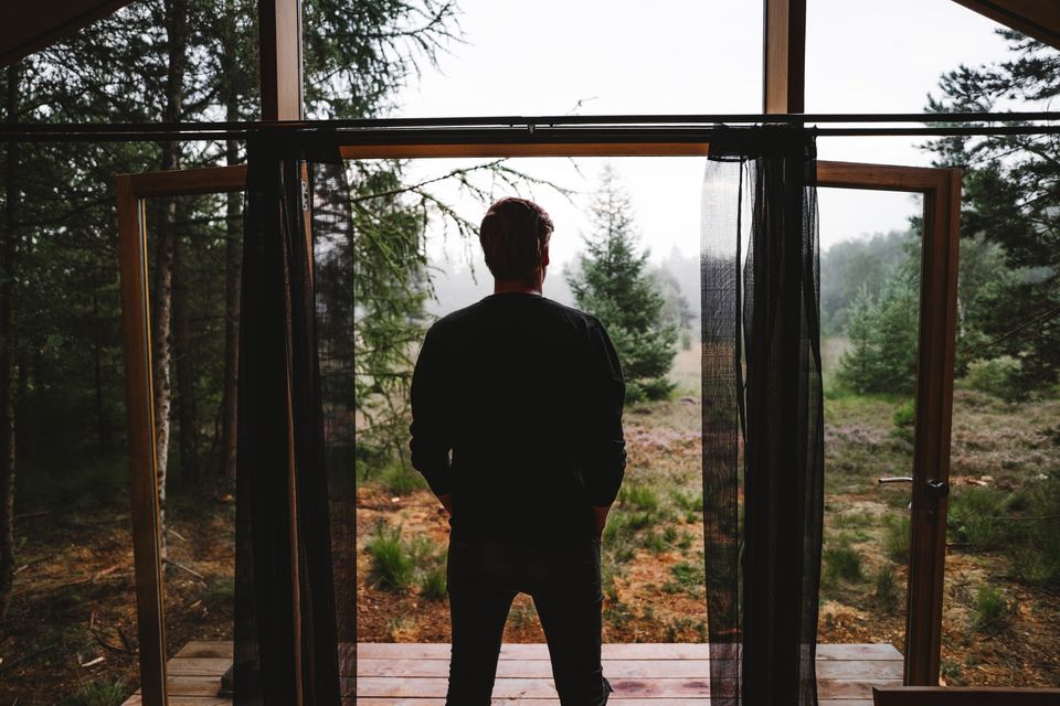 Een man staat in de deuropening van een vakantiehuisje midden in de natuur.