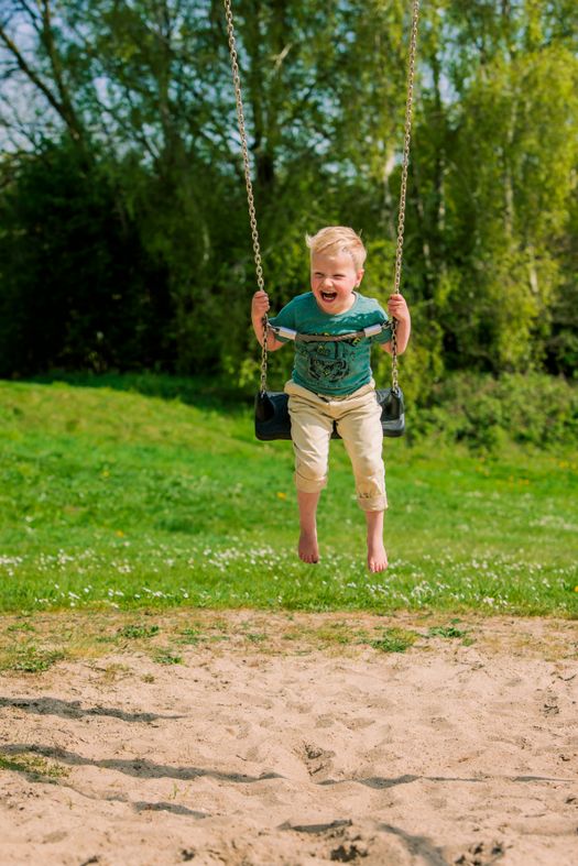 Jongetje zit lachend op een schommel.