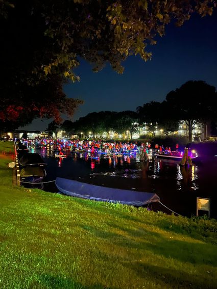 Groep suppers met kleurrijke lampjes op het water tijdens het evenement SUP & Shine in Woerden, sfeervol verlicht in de avond.