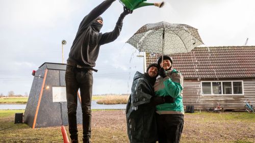 Iemand die water gooit over 2 mensen met een paraplu