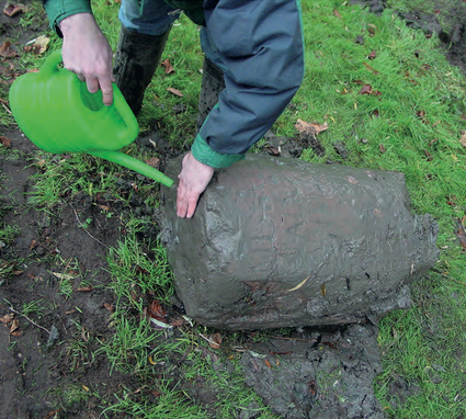 De modder wordt van de zojuist gevonden tweede mijlpaal gespoeld. De eerste letters worden zichtbaar.