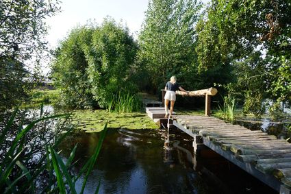 Groepsactiviteit op het blotevoetenpad bij Buitenplaats Kameryck in Kamerik, waar een vrouw over een houten brug door de natuur loopt
