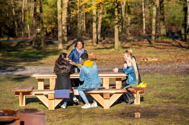 Kinderen en ouders pauzeren op een picknickbank midden in het Drentse bos.