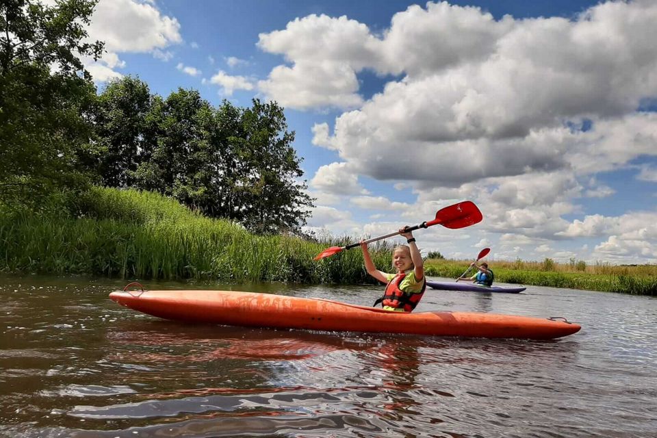 Een meisje zit in een kano op het water en houdt haar peddel boven het hoofd.