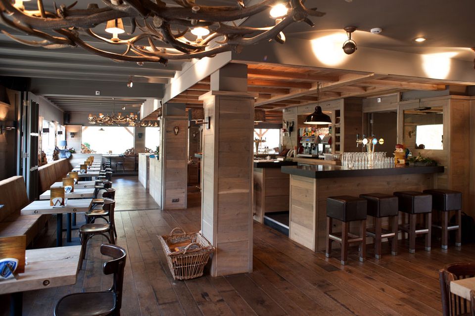 Bar-restaurant met links zitjes en rechts de bar en een lamp gemaakt van geweien.