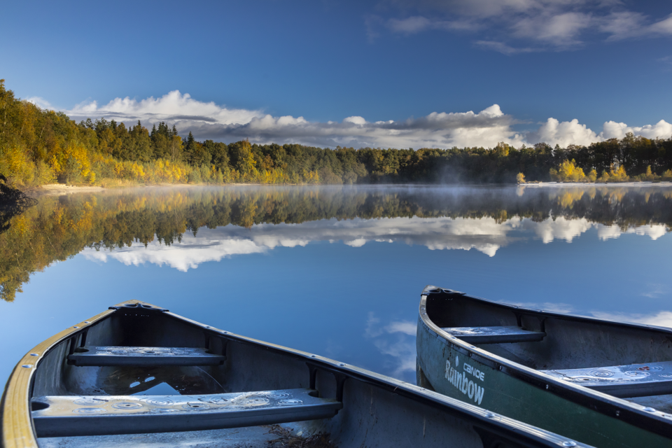 Zwei Boote liegen im Waldsee Ellertshaar, in dem sich der wolkenverhangene Himmel spiegelt und das von einem Kiefernwald umgeben ist