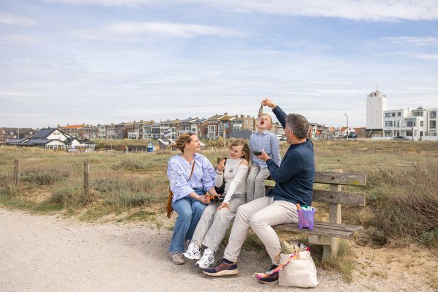 Een jongetje proeft haring, zijn vader houdt de haring omhoog. Op de achtergrond zie je de Vuurbaak.