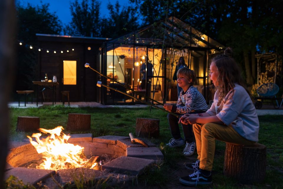 Broer en zus roosteren een marshmallow boven het kampvuur.