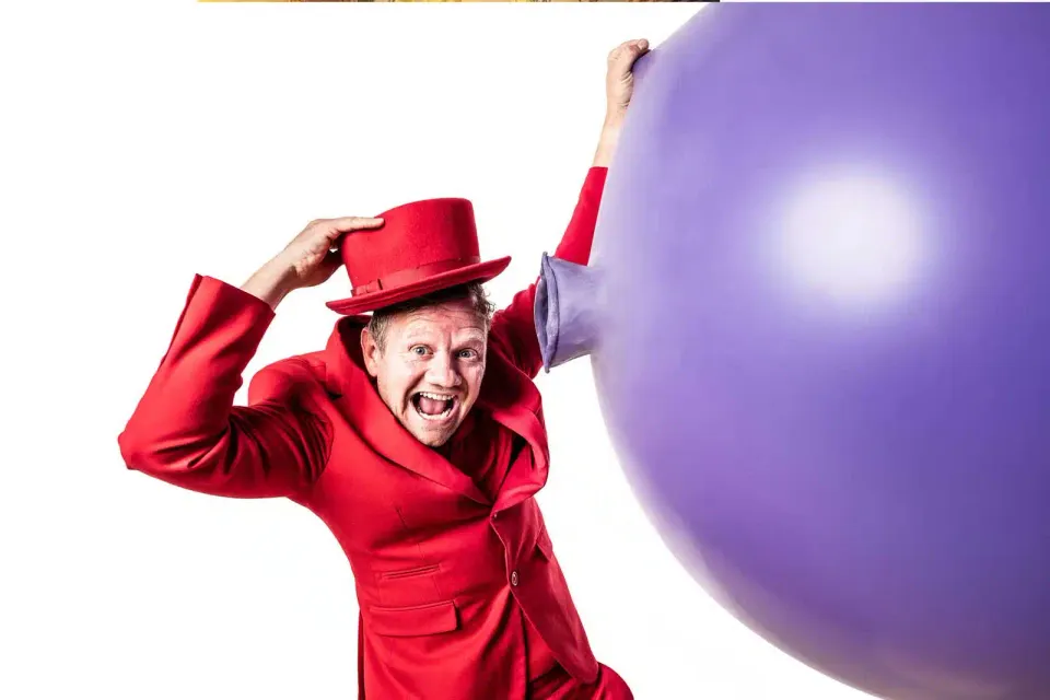 De ballonnenman in een rood pak naast een super grote paarse ballon