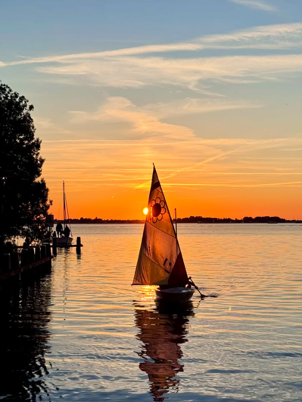 Een zeilbootje komt aangevaren met ondergaande zon.