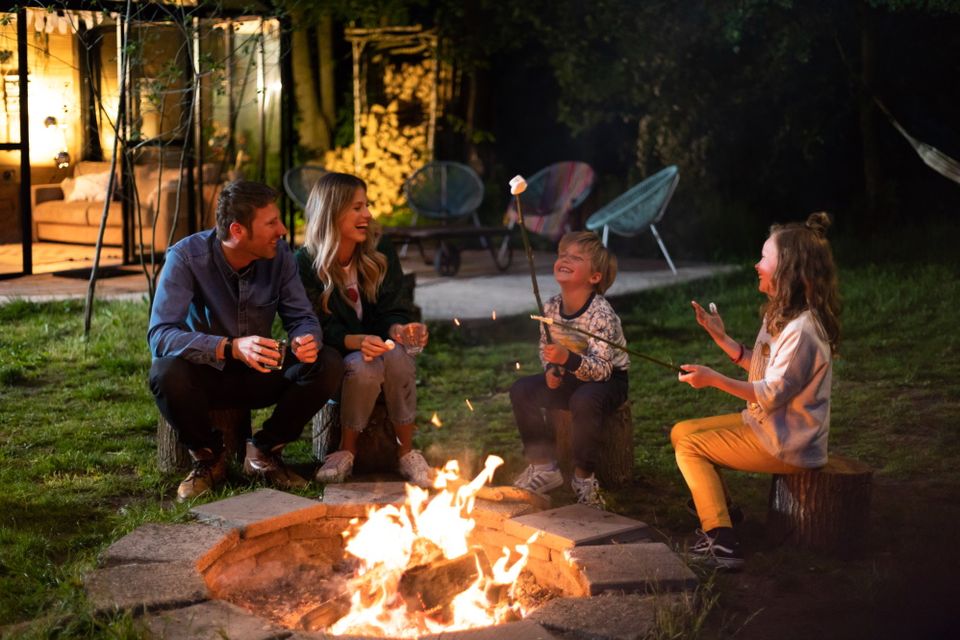 Een gezin zit samen om het kampvuur voor hun vakantiehuisje.