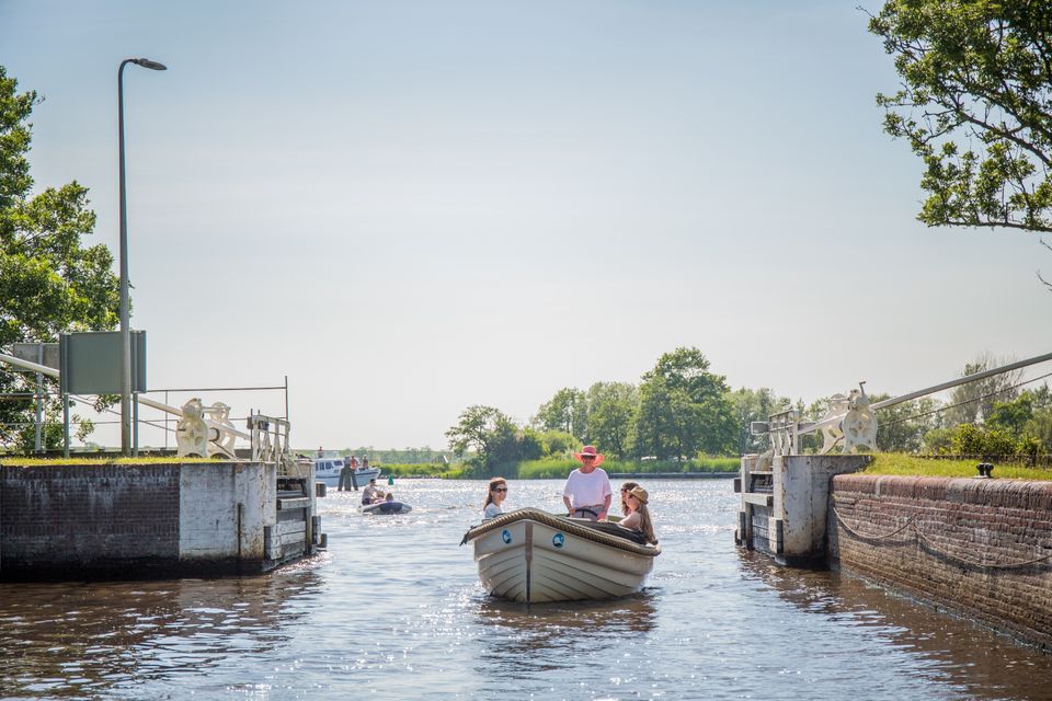 Vier vrouwen varren door een sluis met op de achtergrond een motorbootje en een motorjacht.