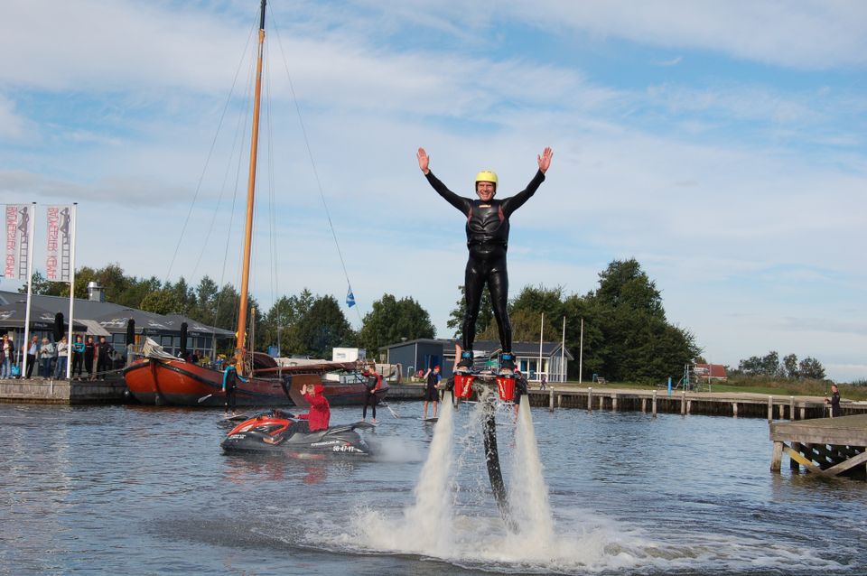 Een man is lachend aan het flyboarden op het water en steekt zijn handen in de lucht.