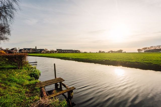 Rustig polderlandschap bij Bodegraven met een houten steiger aan het water, groene weilanden en de zon laag aan de hemel in het Groene Hart.