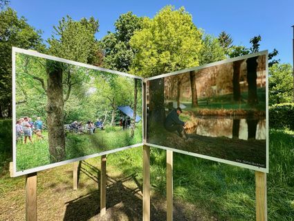Twee grote buitenfoto’s op houten panelen op Landgoed Bredius in Woerden, waarop links een groep mensen in een bosrijke omgeving te zien is en rechts een man zittend bij de waterkant, onder heldere blauwe lucht.