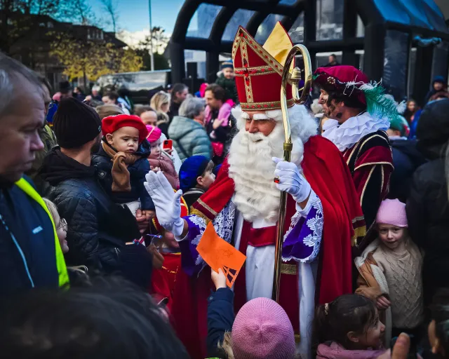 Sinterklaas begroet tijdens zijn intocht de kinderen in een drukke menigte bij het gemeentehuis.