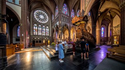 mensen krijgen uitleg bij de preekstoel in de kerk; links een groot rond glas-in-loodraam