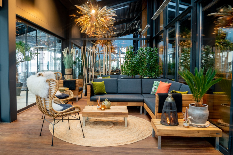 Een gezellig interieur van een restaurant met een lage hoekbank, met houten tafeltjes en een kleed op de grond.