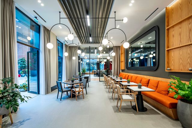 Foto van een industriële inrichting van de bar met een lange oranje bank aan de rechterkant en veel kleine zitjes.