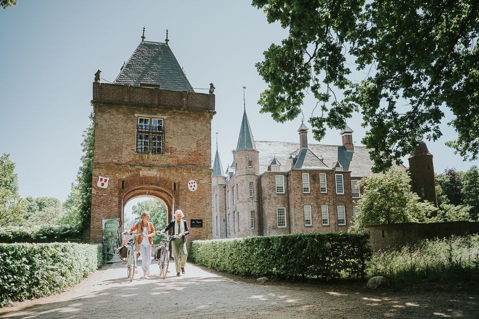 Twee vriendinnen lopen met de fiets aan de hand onder het poortgebouw van Slot Zuylen door