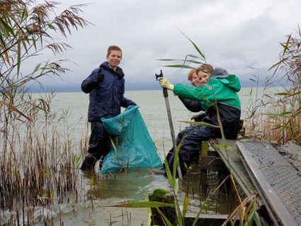2 jongens in het water met vuilniszakken in de hand.
