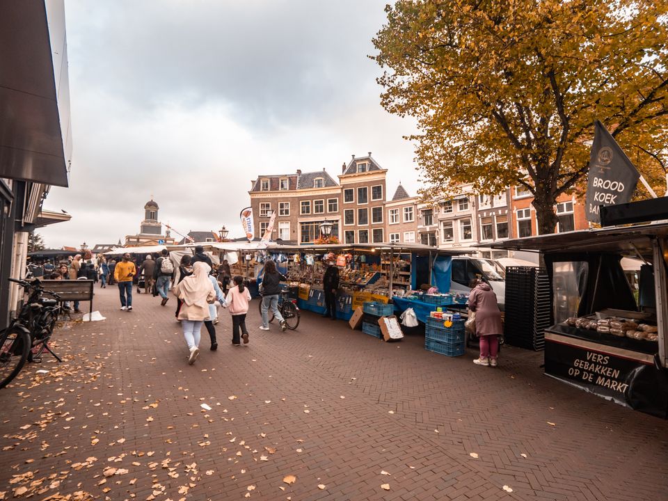 Sfeerbeeld van de eeuwenoude zaterdagmarkt in Leiden, winkelende mensen op de Vismarkt met grachtenhuizen op de achtergrond.