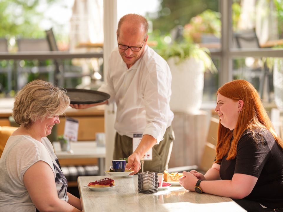 Een man seveert koffie aan een tafel met twee vrouwen.