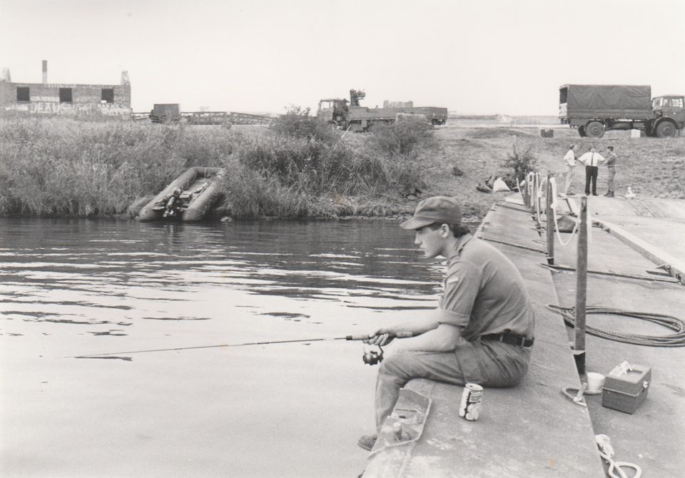 Een visser zit op de pier van Pampus. Op de achtergrond zijn militaire wagens te zien.