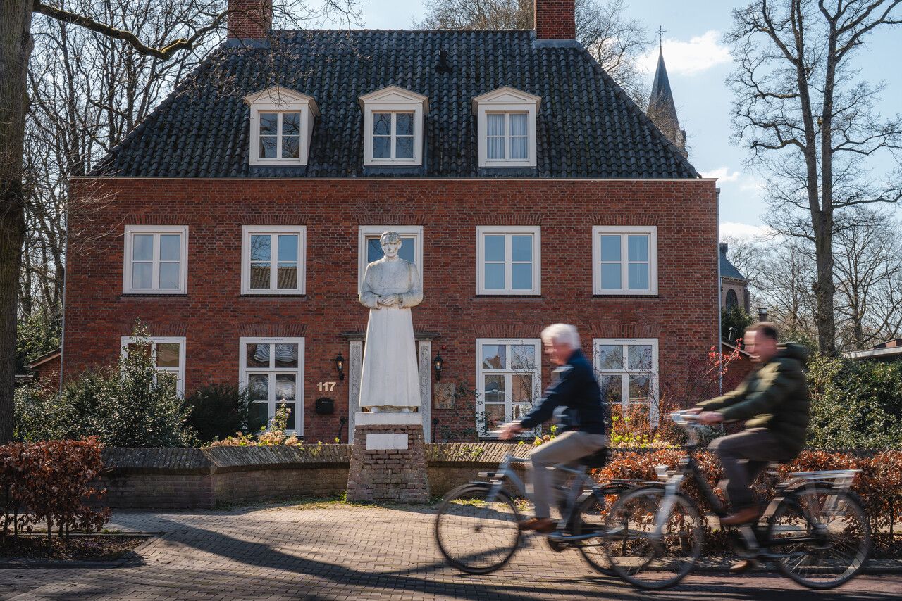 Twee fietsers fietsen langs het monument van Pastoor Bastiaansen