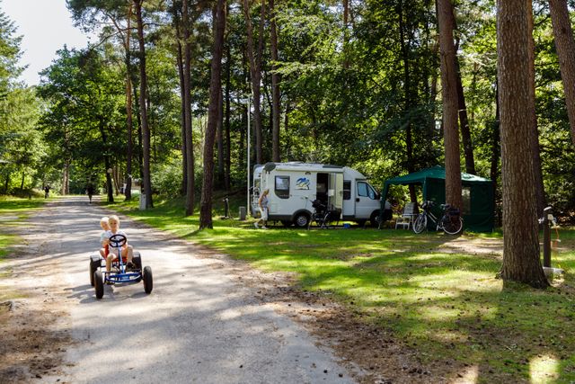 Kinderen rijden op een skelter langs een kampeerplaats met camper bij RCN het Grote Bos. De bosrijke camping biedt ruime plekken midden in de natuur.
