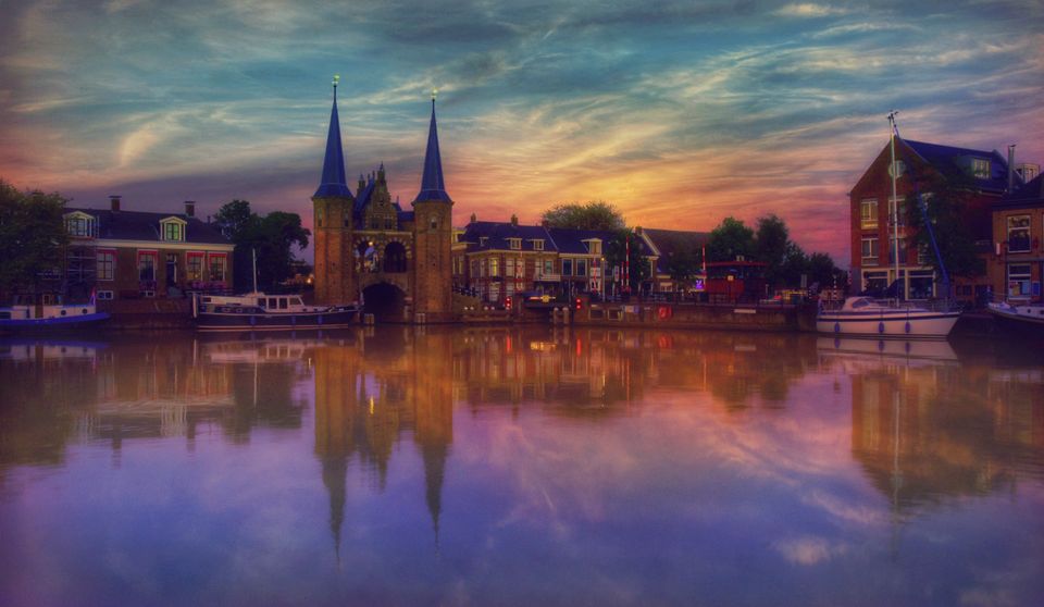 Foto van de Waterpoort in Sneek bij avondlicht, de lucht kleurt blauw, geel en roze, het water paars.