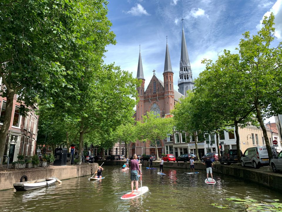 Historische binnenstad Gouda in het Groene Hart met suppers op de gracht bij de Gouwekerk tijdens een zomerse dag tussen monumentale panden en groene bomen langs het water.