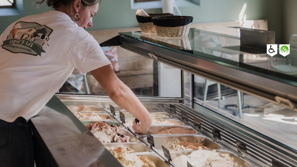 IJswinkel Lieke’s IJs Woerden, provincie Utrecht, Groene Hart, medewerker in T-shirt met logo schept vers bereid boerderij-ijs in verschillende smaken uit een gekoelde ijsvitrine.