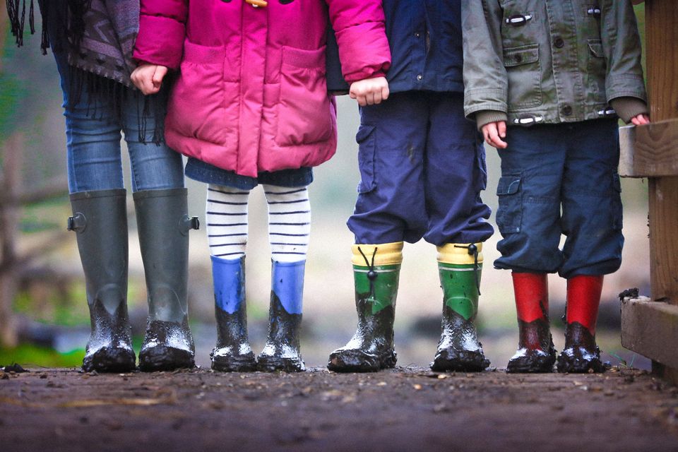 Een vrouw en drie kinderen staan buiten op een rijtje. Ze hebben allemaal regenlaarzen aan die onder de modder zitten.