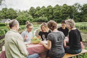 Groep mensen die aan een tafel aan het eten zijn. Deze tafel staat buiten in de tuinderij.