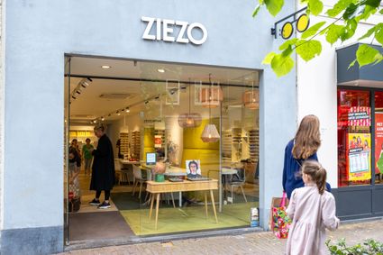 Lichtgrijze gevel, grote glazen pui met letters Ziezo erboven en winkelend publiek.