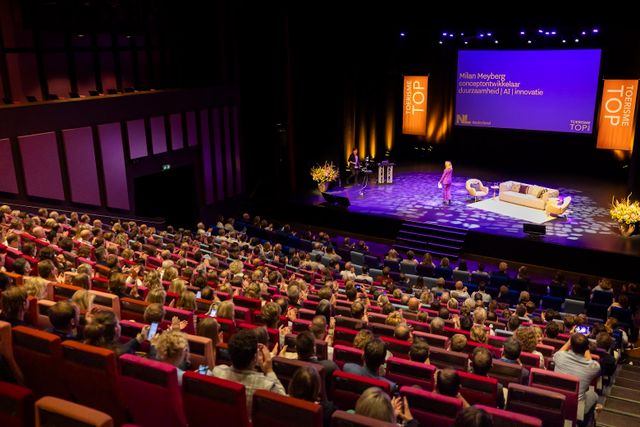 Publiek in theaterzaal luistert naar sprekers op het podium tijdens de Toerisme Top 2024 in Venlo.